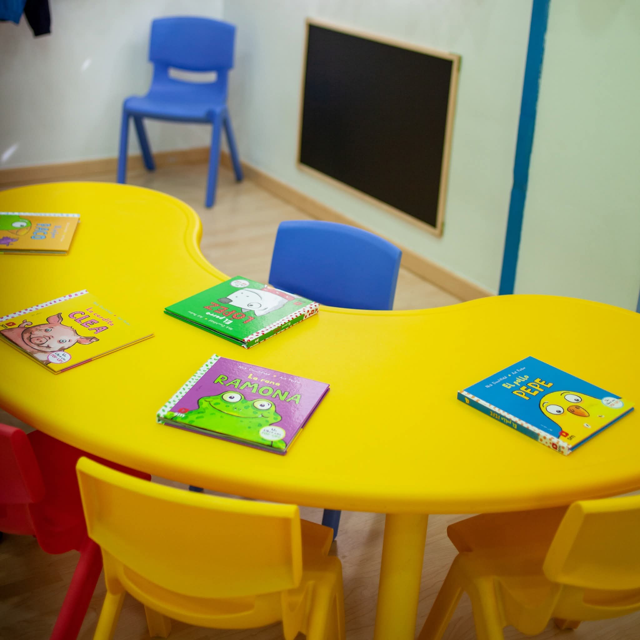 Rincón de lectura con libros infantiles, mesa amarilla y sillas azules en CEI Caracola Utrera.