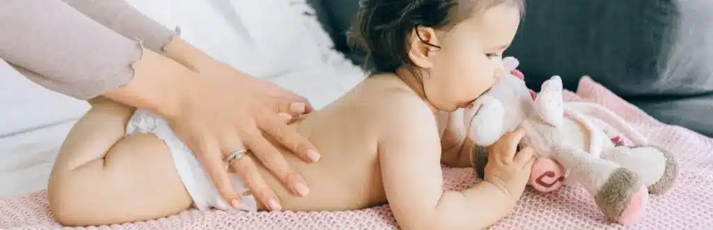 Niña pequeña tumbada mientras le cambian el pañal. Cómo quitar el pañal y control de esfinteres en niños.