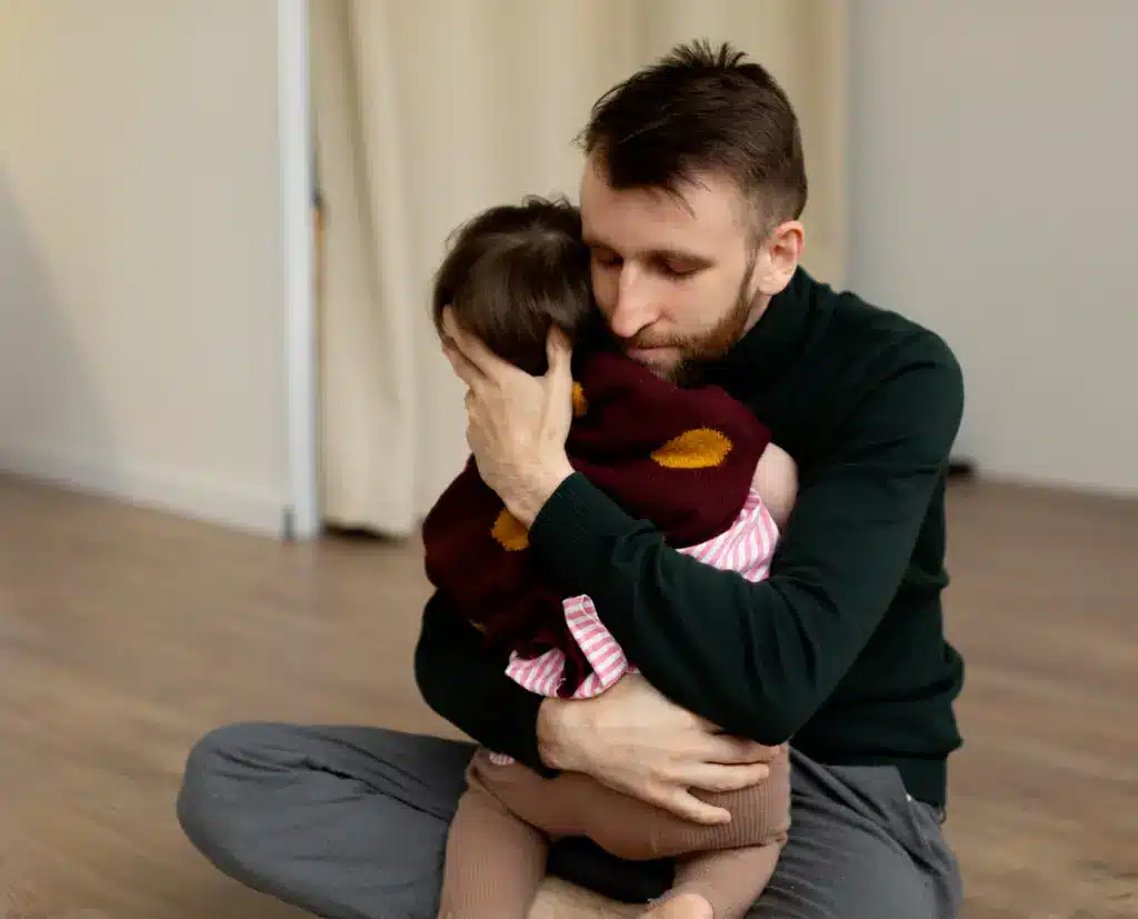 Padre abrazando a un niño pequeño durante un momento de llanto y desregulación emocional. Rabietas niños 2 años.